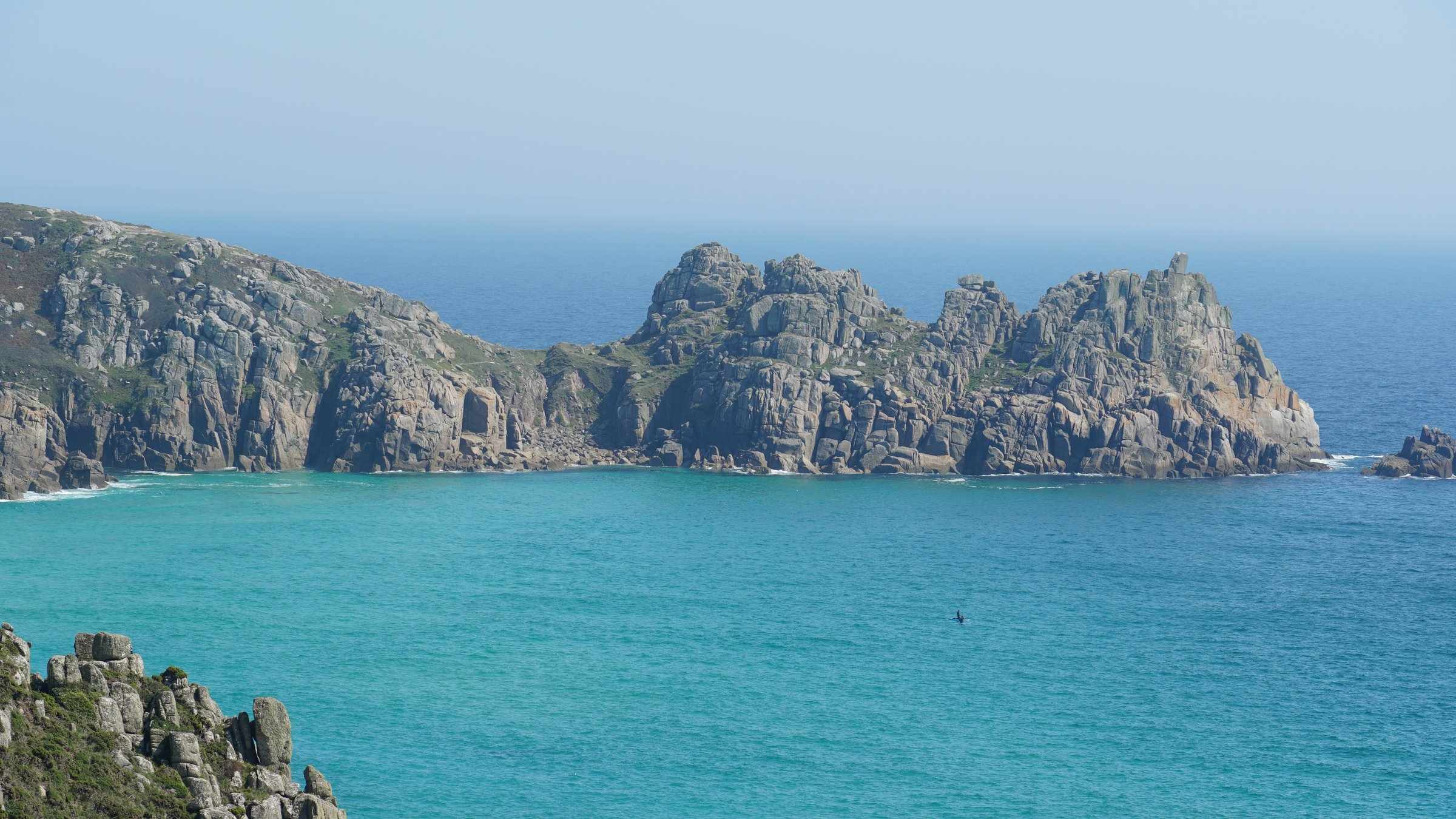 Turquoise water and white sand at Porthcurno Beach, framed by granite cliffs on the south Cornwall coast.