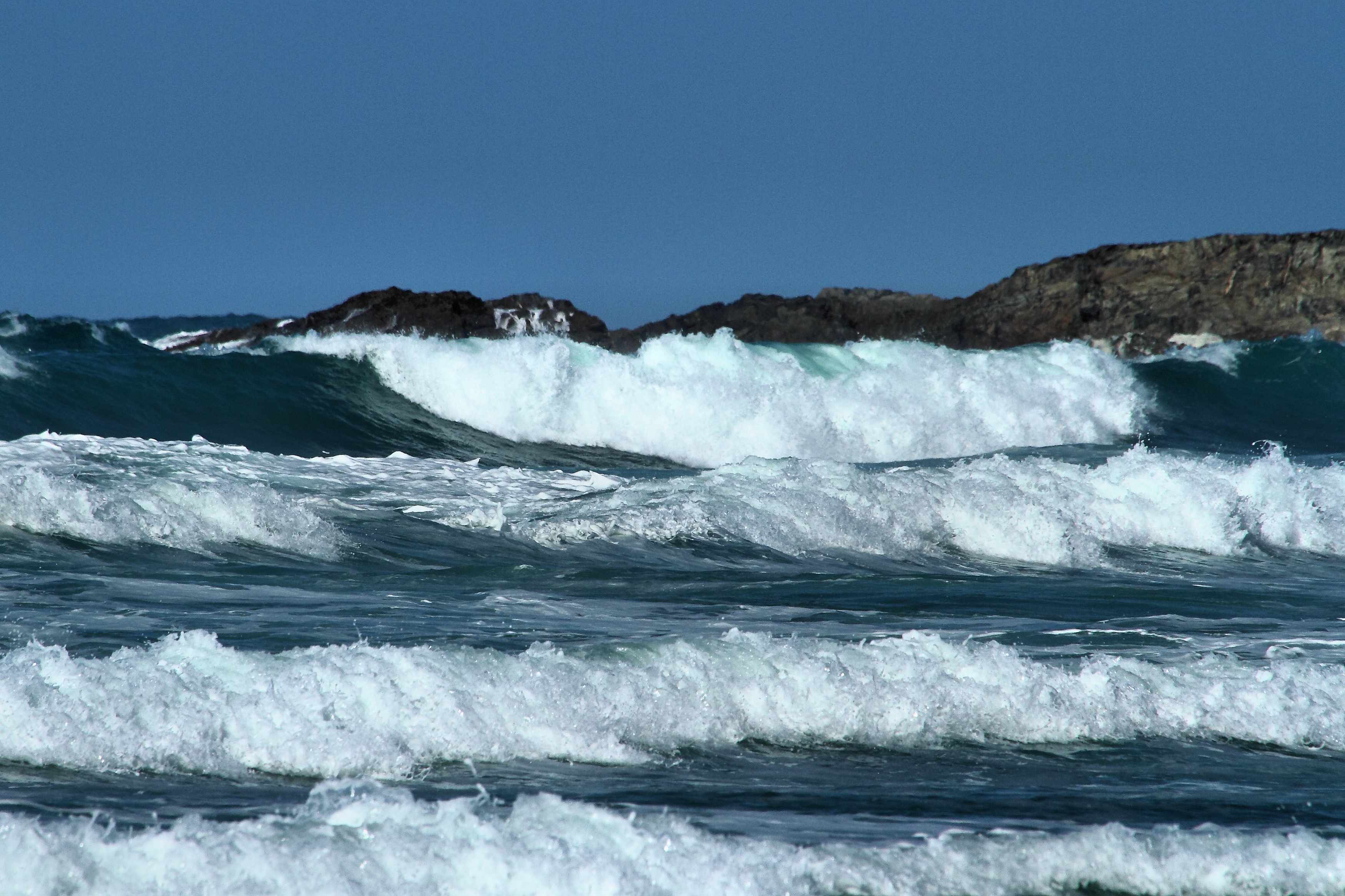 A beginner surfer riding whitewash on a wide Cornish beach — blue sky, clean waves, and the glow of a good first session.