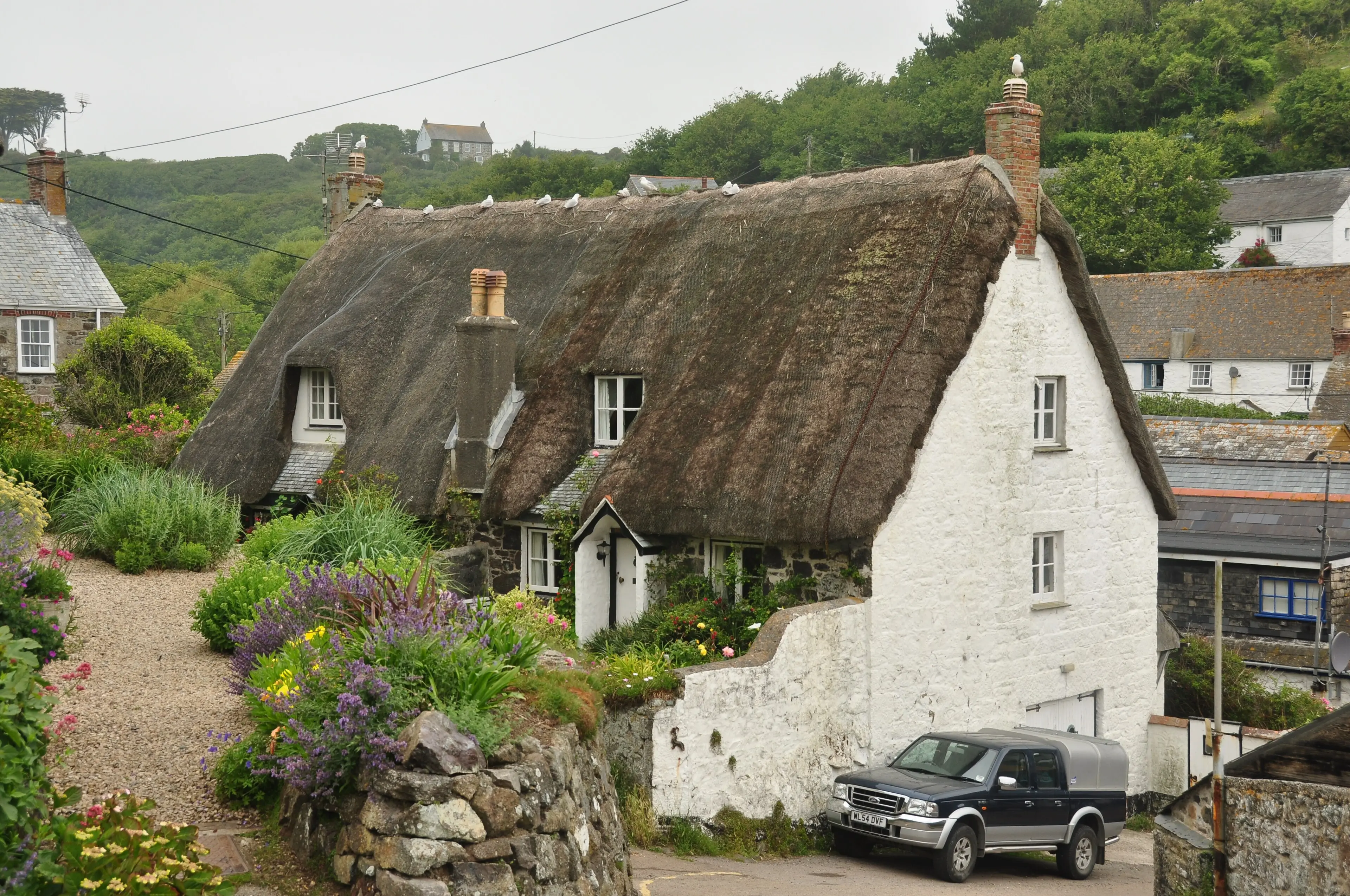 Cadgwith village on the Lizard Peninsula — thatched cottages above a small fishing cove with boats on the beach.