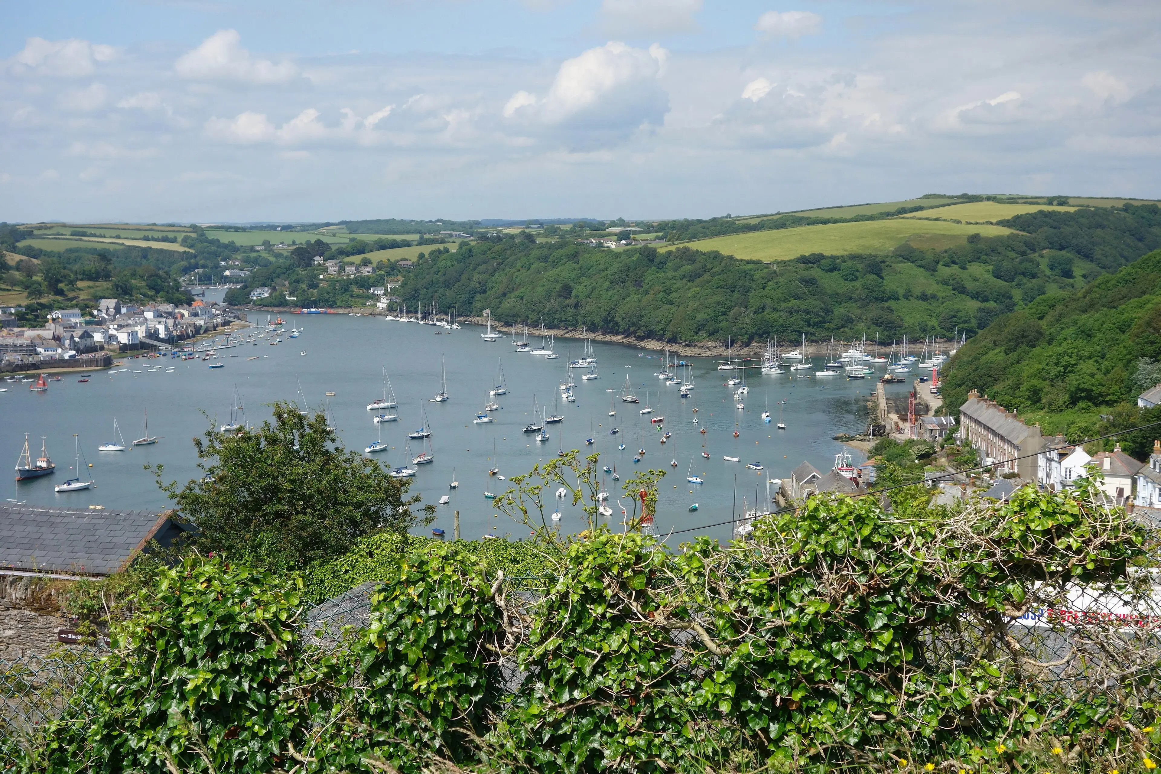 Fowey harbour — colourful houses climbing the hillside above the deep-water estuary, sailing boats at anchor.